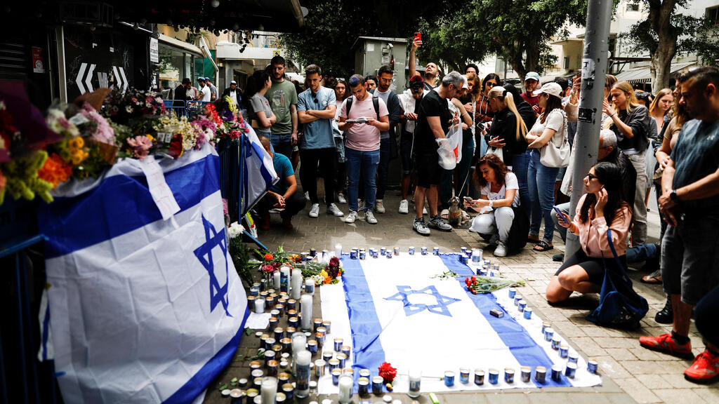 People lighting candles and placing flowers in memory of the three civilians murdered in the terror shooting in Tel Aviv (Photo: Reuters) אנשים הגיעו להדליק נרות ולהניח פרחים בזירת הפיגוע