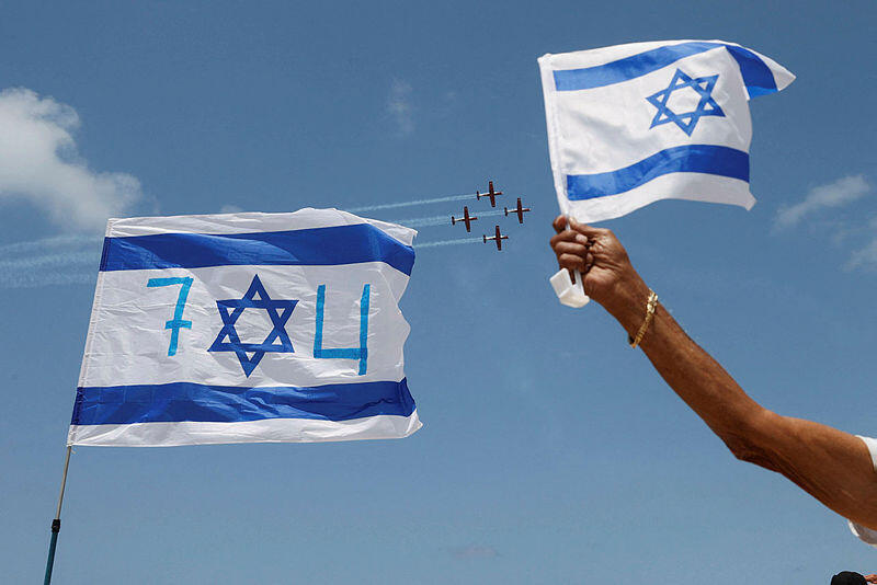 Israeli flag being waved as Independence Day flyover is seen in the background (Photo: AFP) יום עצמאות העצמאות 74 מדינה מדינת ישראל דגל מגן דוד מטס מטוסים מטוס חיל האוויר