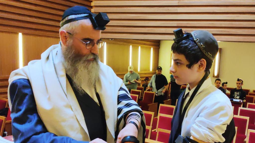 Rabbi Avraham Wolf assists boy with putting on Tefillin (Photo: Liat Mia Lombrozo) הנחת תפילין לאחד הילדים