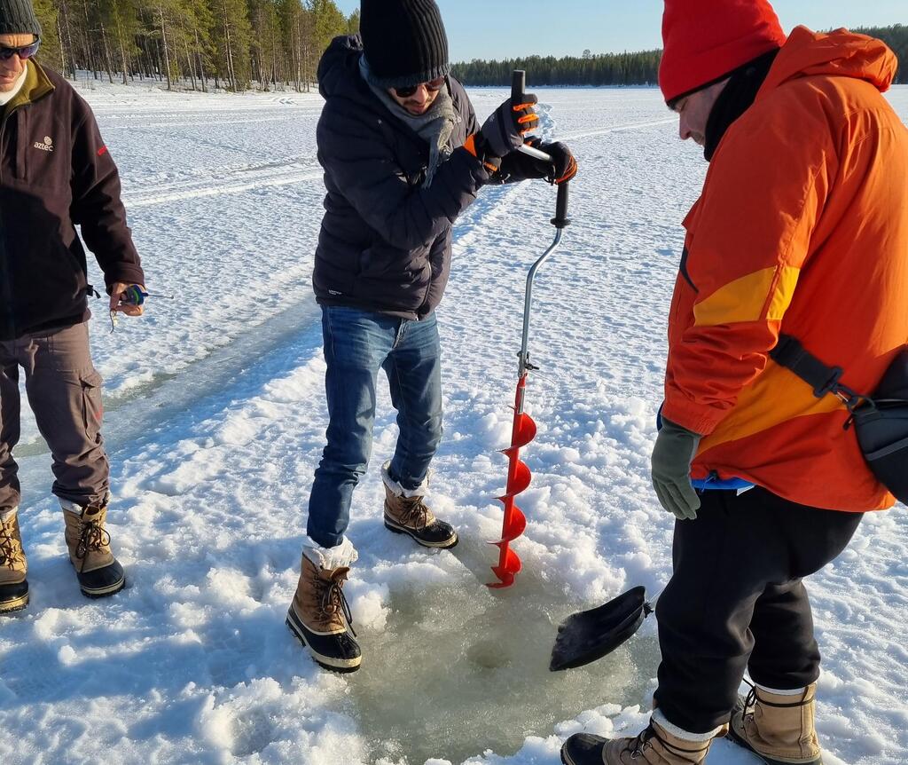 מנסים לדוג עם חכה באגם הקפוא, דרך קרח בעומק של שלג