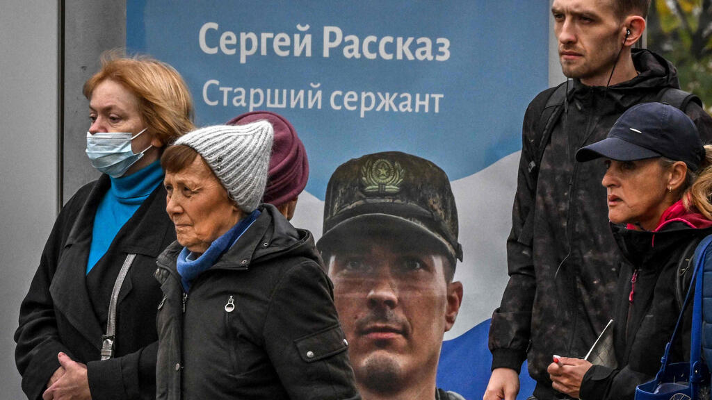 Russians walks past a billboard displaying a Russian soldier with a slogan reading 'Glory to the Heroes of Russia' 