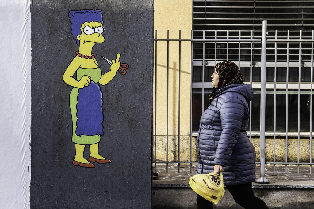 ציור קיר במילאנו, איטליה, לאות הזדהות עם האיראניות: מארג' סימפסון גוזרת את שיערה, מעשה שנחשב לאחד מסמלי המחאה, ומפנה אצבע משולשת לאייתוללות (צילום: EPA) איטליה מילאנו ציור קיר הזדהות עם מחאת ה חיג'אב ב איראן מארג' סימפסון גוזרת את שיערה ומפנה אצבע משולשת