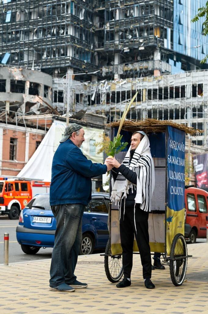 Mobile sukkah in Ukraine against the backdrop of buildings damaged in Russian bombardments (Photo: Artur Kuzalov) סוכה של בית חבד ברקע ההריסות באוקראינה: הסוכות הנודדות של חב"ד