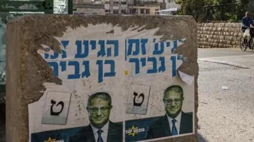 A man cycles near a concrete block bearing posters depicting far-right Israeli MK Itamar Ben Gvir, in the West Bank city of Hebron 