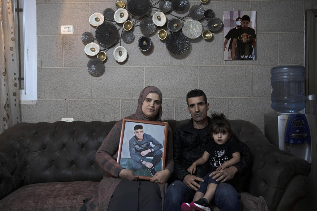 Maysoon, left, and Saleh Manasra pose for a portrait with their daughter, Sham, in their home in East Jerusalem, Nov. 8, 2022 (Photo: AP) Manasra's parents shwing his picture