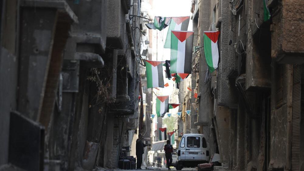 People walk under Palestinian flags in Yarmouk camp in Damascus Syria that has seen heavy fighting during the civil war, Wednesday, Nov. 2, 2022 