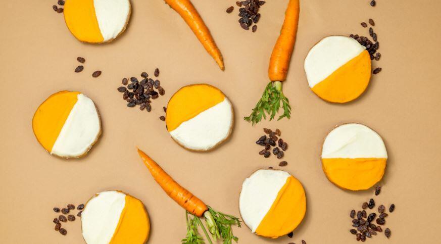 A carrot cake flavored cookie is topped with orange and white cream cheese frosting.