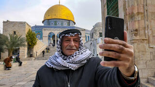 A man uses his phone to take a 'selfie' photo with the Dome of the Rock shrine