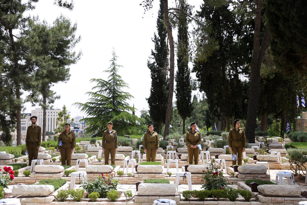 Israeli soldiers stand guard among fallen Israeli soldiers' graves as they decorate them with small Israeli national flags at the Mount Herzl military cemetery in Jerusalem, Israel, 23 April 2023 