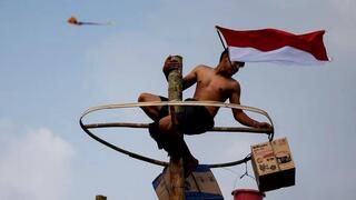 A man holding Indonesian flag with his mouth, reaches for the prizes on top of a greased pole during "Panjat Pinang" competition in celebrating  country's 77th Independence Day, in Jakarta, Indonesia