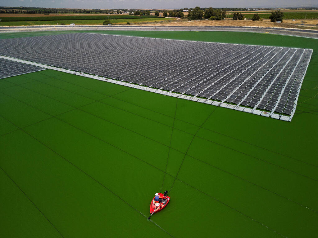 An aerial view shows workers installing solar panels on a water reservoir