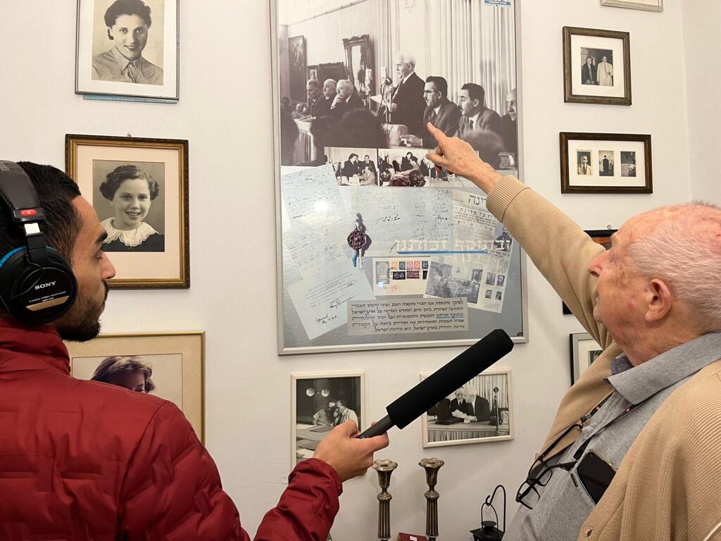 Moshe Inbar, the son of Peretz Bernstein, a signatory of Israel’s Declaration of Independence, points to his father in a picture from the signing ceremony, while “Israel Story” producer Jamal Risheq records him 