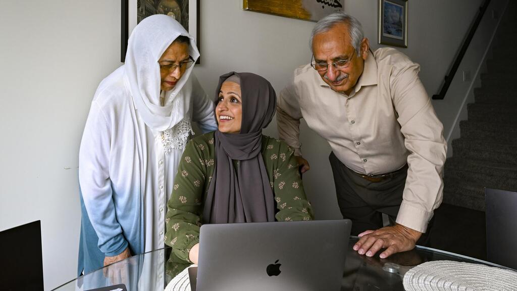 Muslim family members Saadiha, seated, Saeeda, and Abdul Khaliq, right, gather around a computer which they use to research for their hajj trip 