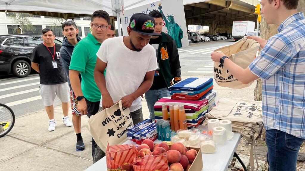 Men who are staying at "The Hall," one of New York's largest migrant shelters, fill bags with toiletries and fresh fruit in a tent staffed by Masbia Relief 