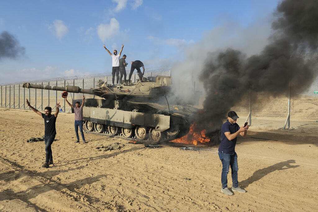 במהלך מתקפת חמאס ב-7 באוקטובר (צילום: AP Photo, File) ארכיון מחבלים פלסטינים חוגגים על טנק עולה באש
