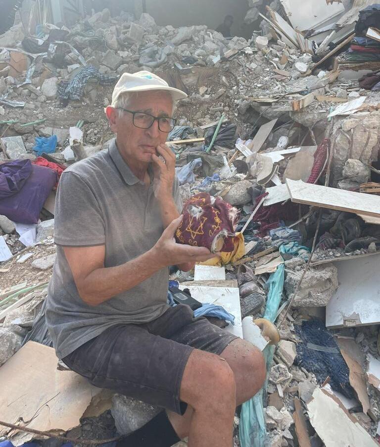 Shai Hermesh holding tefillin on the ruins of his home שי חרמש עם התפילין ששרדו את מתקפת הטרור של חמאס