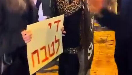 מפגינה מניפה שלט "די לטבח" בקפלן