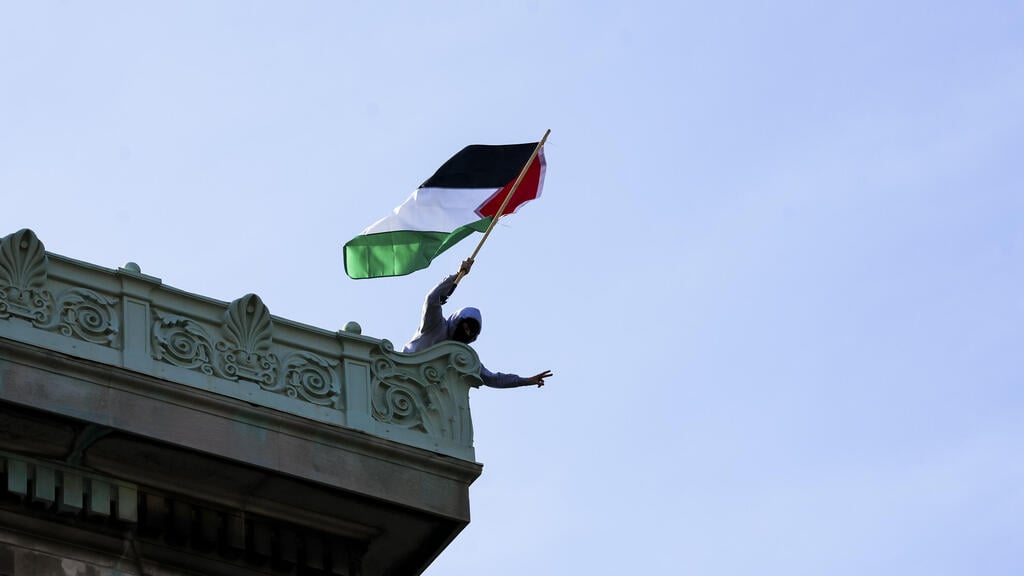 A protester waves Palestinian flag during student occupation of Columbia University building (Photo: Stephani Spindel / EPA) מפגין פרו-פלסטיני על גג בניין המילטון