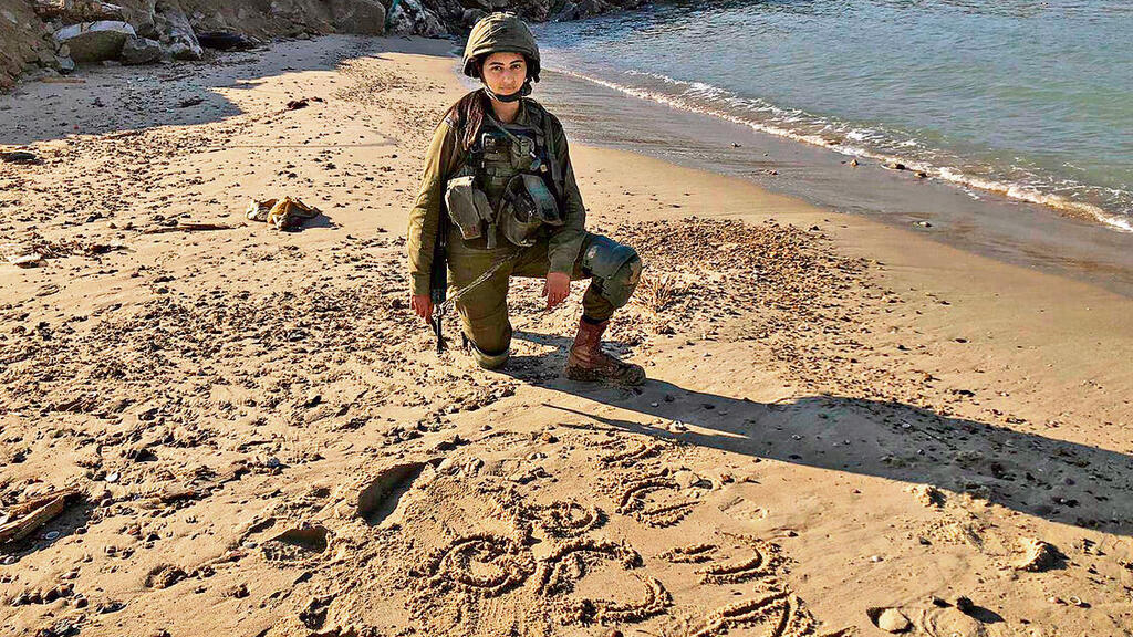 רב"ט מיקה נקש על חוף עזה, שמותיהם של אחיה כתובים בחול (צילום: דובר צה"ל) yk13915448