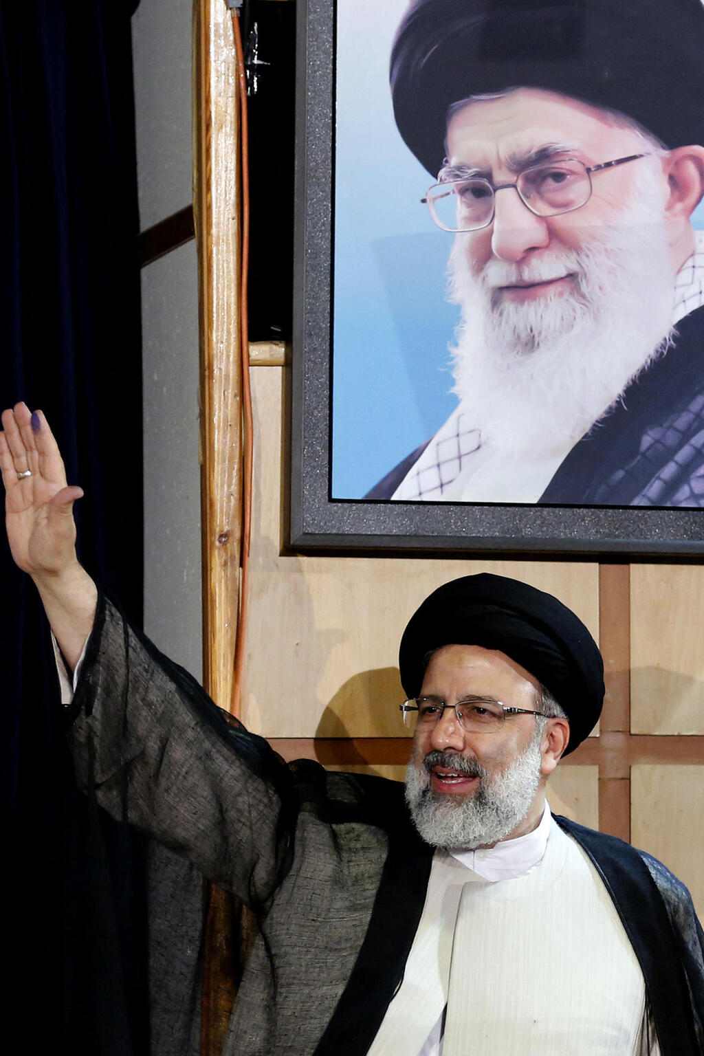 Ebrahim Raisi stands under a portraait of Iran's Supreme Leader Ali Khamenei (PHoto: Atta Kenare / AFP) נשיא איראן שנהרג ב התרסקות איבראהים ראיסי לצד תמונת המנהיג העליון חמינאי בשדנת 2017 - כשראיסי התמודד אז (ונכשל) בבחירות לנשיאות