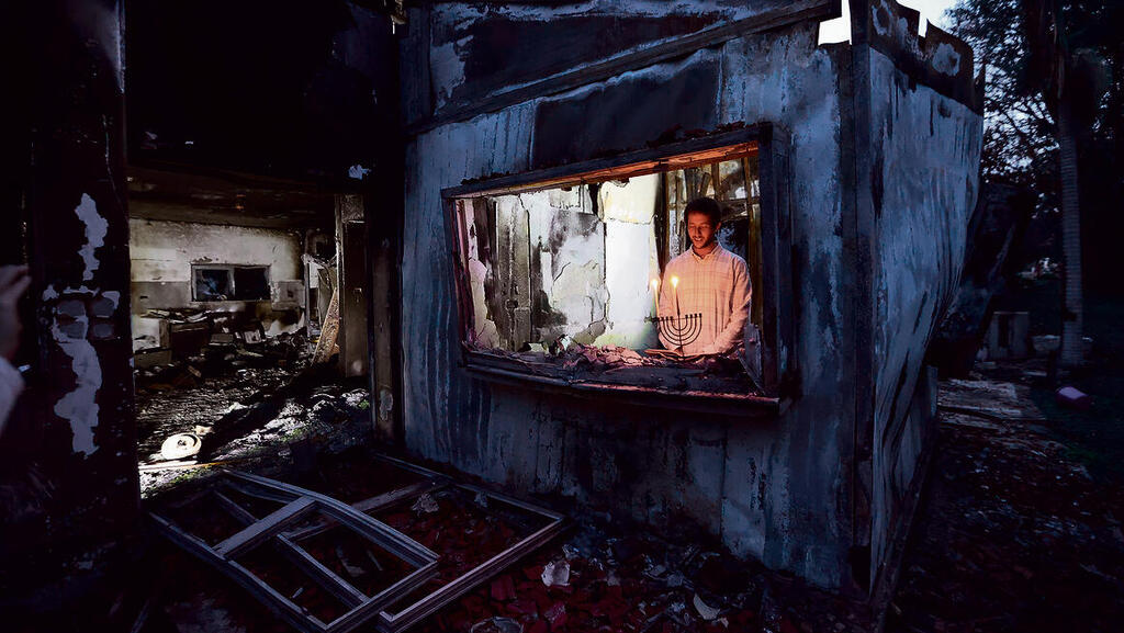 תמיר הרשקוביץ מברך על הנרות, בחנוכייה שנותרה שלמה בהריסות בית הוריו בבארי | צילום: גדי קבלו yk14089884