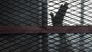 A member of the Muslim Brotherhood waves his hand from a defendants cage in a courtroom in Torah prison, southern Cairo, Egypt 