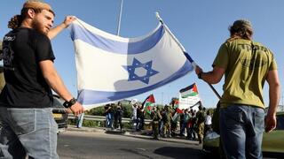 Israeli security forces stand between Jewish settlers and Palestinians, accompanied by Israeli and foreign activists, each side carrying their flags in West Bank