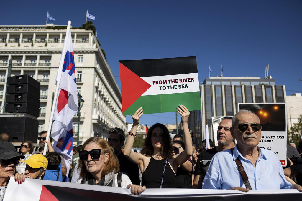 "משמעות הסלוגן 'מהנהר לים' היא חיסול המדינה שלנו" (צילום: AP / Yorgos Karahalis) מפגינה באתונה אוחזת שלט שעליו נכתב "מהנהר לים"