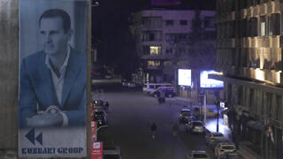 A giant banner of Syrian President Bashar Assad hangs on the facade of a building, as pedestrian walk through an the empty streets of Damascus