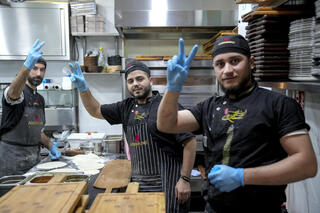 Syrian refugees flash the victory sign to support free Syria while working in a Syrian restaurant in Berlin