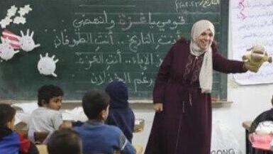 מורה בבית ספר מלמדת ילדים עם בובה לצד לוח עם תוכן שמאדיר את טבח ה-7 באוקטובר