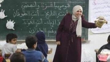 מורה בבית ספר מלמדת ילדים עם בובה לצד לוח עם תוכן שמאדיר את טבח ה-7 באוקטובר