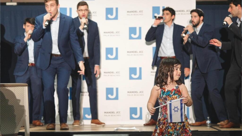 A young girl waves an Israeli flag while a cappella group members perform at a celebration organized by the Mandel JCC of Palm Beach 