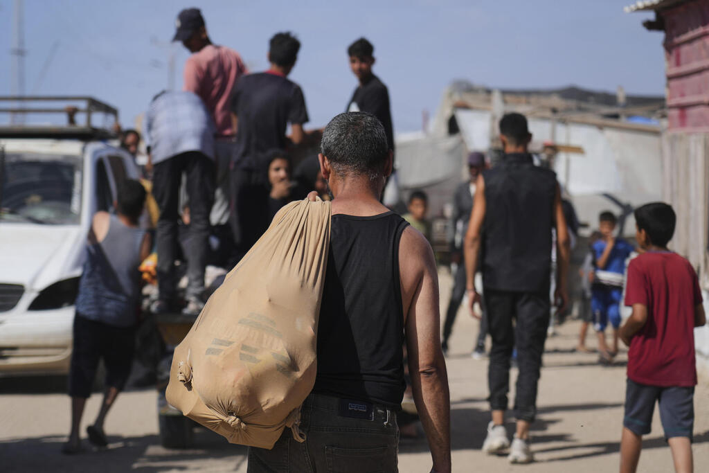 עזתים הולכים לקבל חבילות סיוע המוניטרי ברפיח (צילום: AP Photo/Abdel Kareem Hana) עזתים הולכים לקבל חבילות סיוע המוניטרי ברפיח