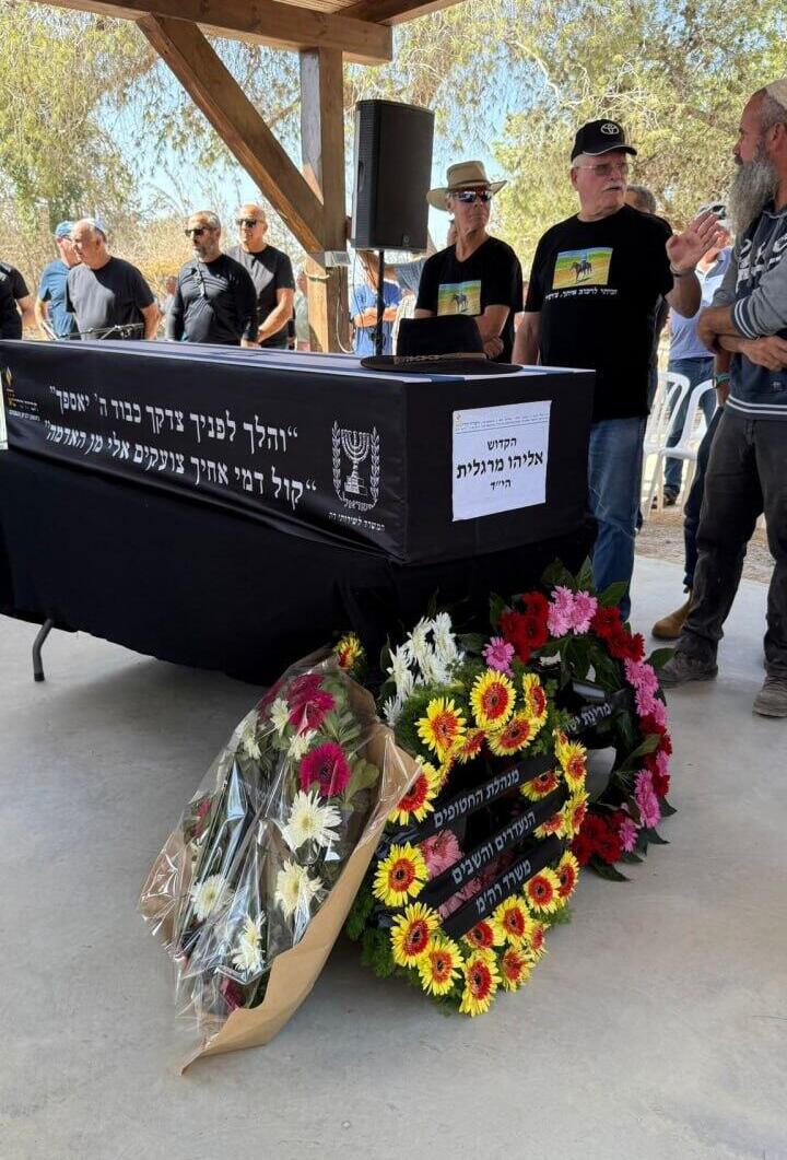 הכובע של "צ'רצ'יל" על ארון הקבורה (צילום: דוברות ניר עוז) נילי מרגלית מניחה על ארונו של אביה, אליהו (צ'רצ'יל) מרגלית, את כובעו