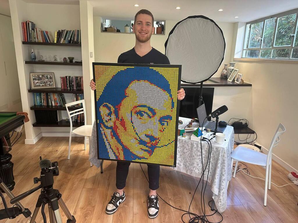 Rubik’s Cube artist Tom poses with a completed portrait of Salvador Dalí made entirely of rotated cubes in his home studio. Each work uses hundreds of cubes to recreate iconic faces, blending mathematical precision with artistic expression 