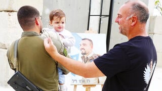 רס"ן ר' עם התינוקת רון והאב השכול רוני פרץ, על רקע תמונתו של רז ז"ל