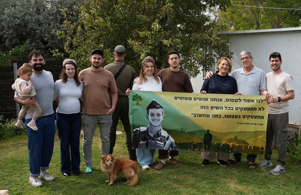 משפחת אלבוים בחצר ביתם כיום, עם כרזה לזכר שריה ז"ל | צילום: אפי שריר